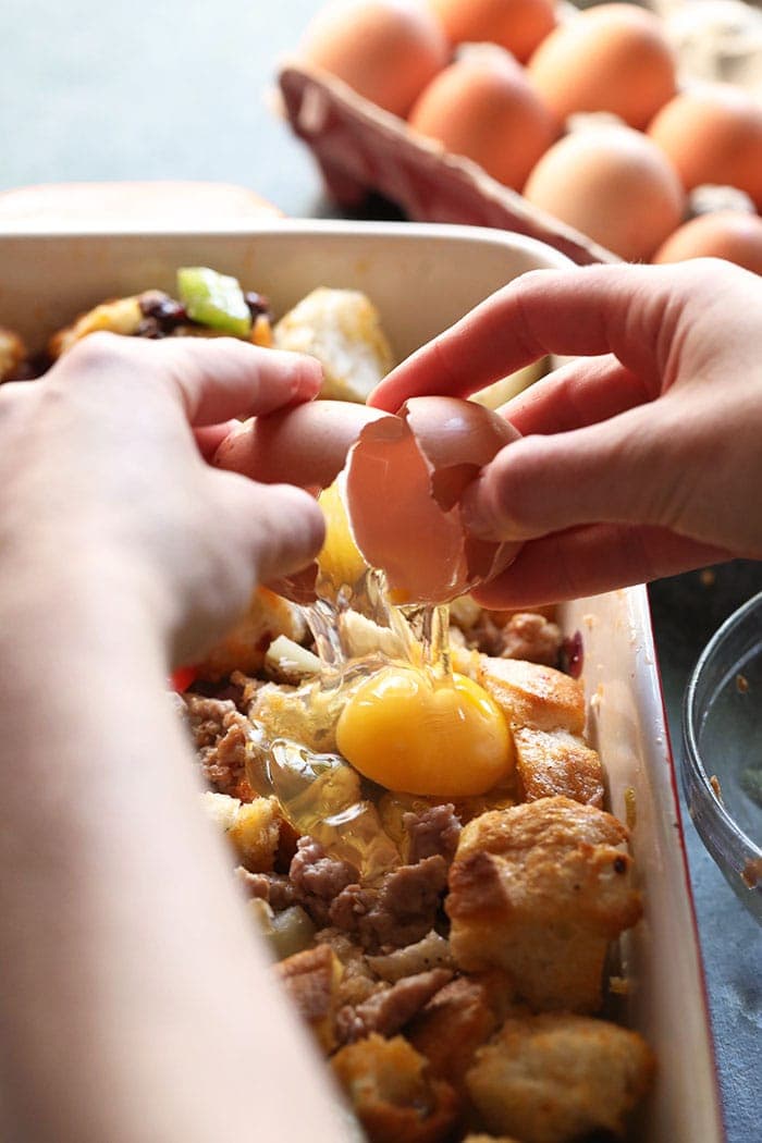 two hands cracking an egg onto casserole mixture