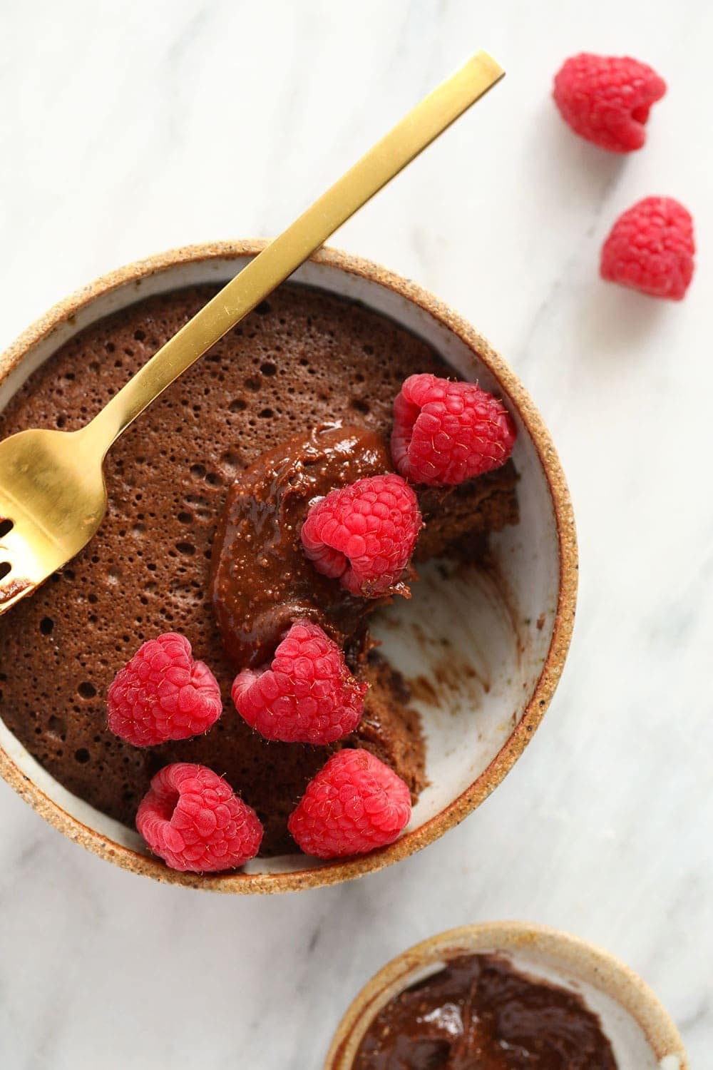 single-serve chocolate mug cake with a bite taken out of it and topped with delicious fresh raspberries