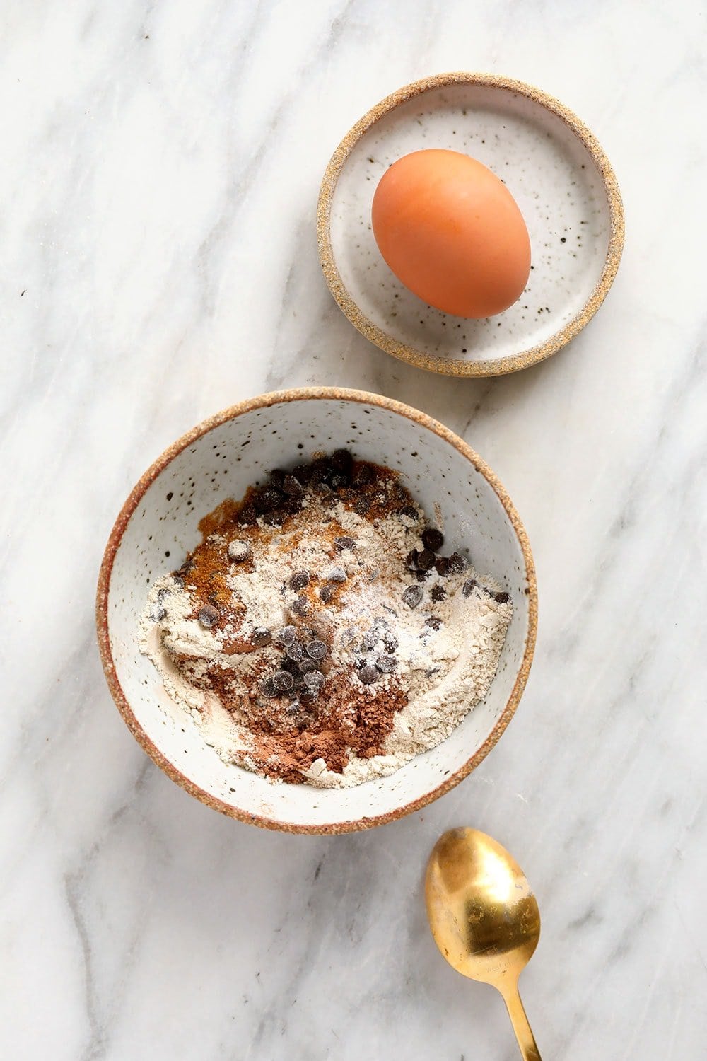 chocolate mug cake dry ingredients in a bowl with an egg ready to be cracked into the mix