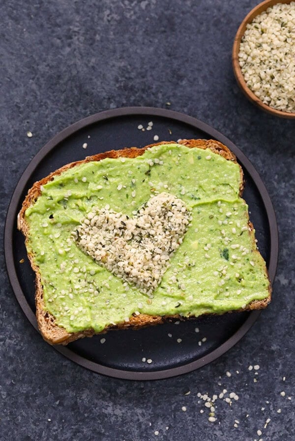 black plate with heart-shaped avocado seeds on top of avocado spread.