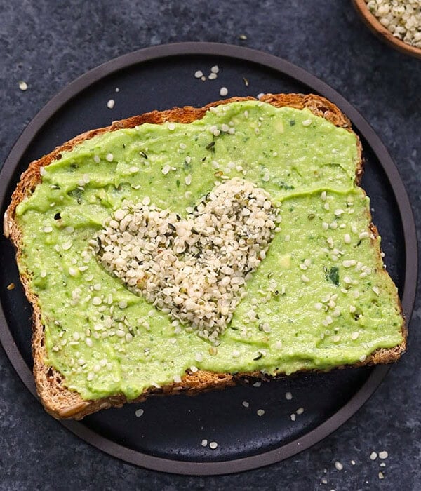 Heart shaped avocado toast with a spread on a plate.