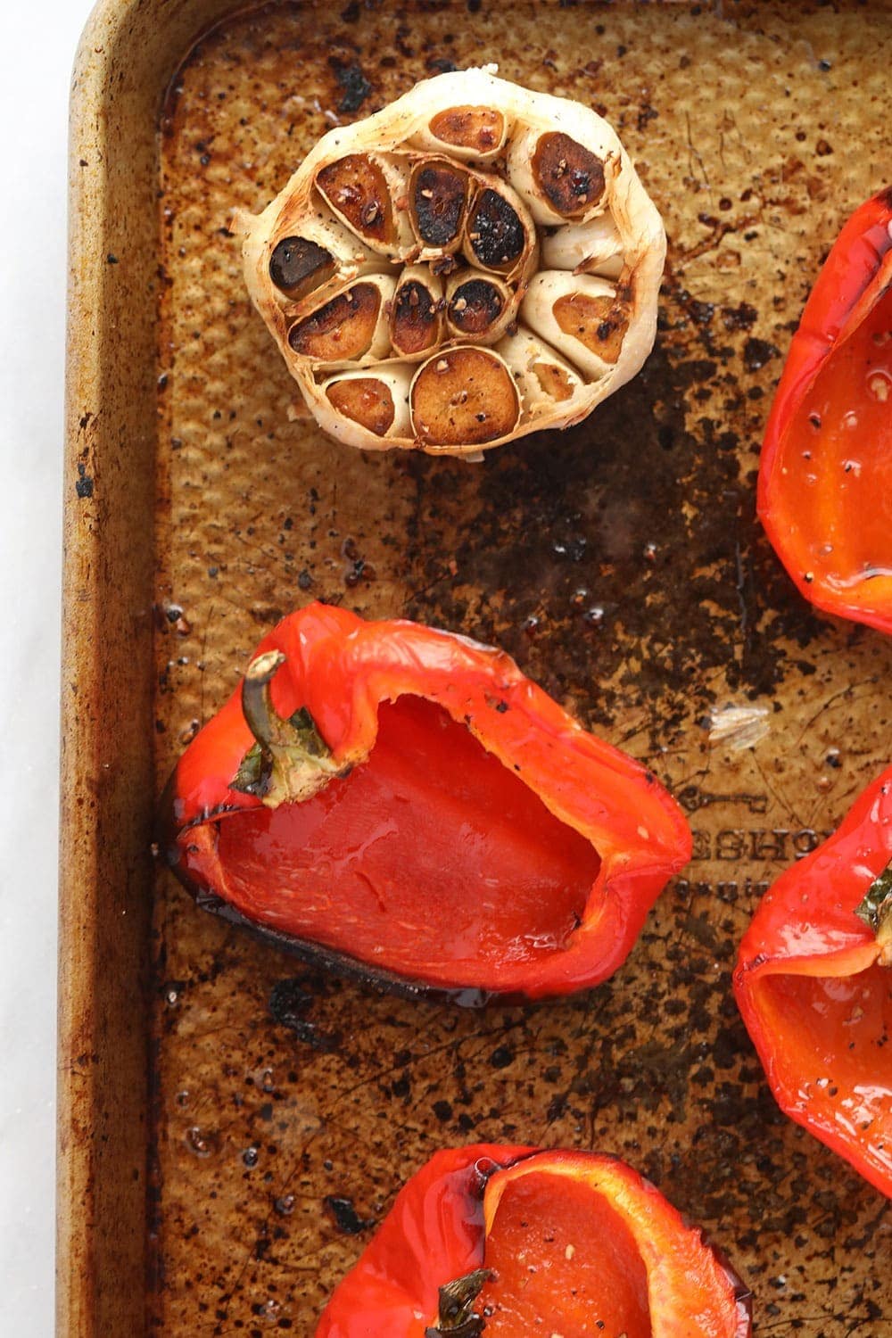 red peppers and garlic cloves ready to be roasted on a baking sheet