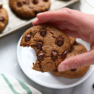 a hand holding a paleo cashew butter cookie with a bite taken out of it.