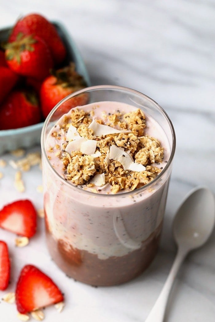 Overhead photo of Neapolitan overnight oats served in a glass jar with strawberries in the background.