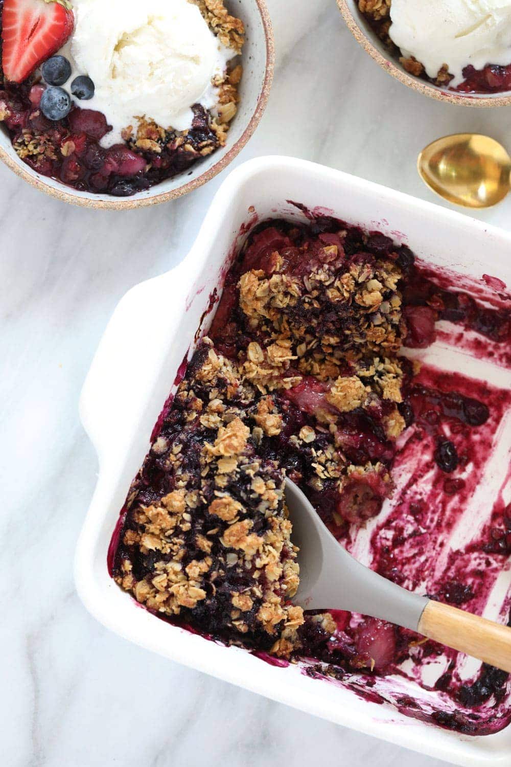 berry crumble in a white dish with serving spoon