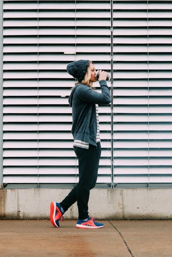 A woman wearing a beanie is sprinting in front of a wall during her strength workout.