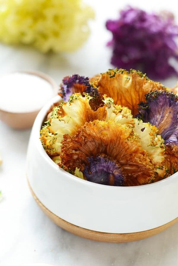 a white bowl with dried cranberries and purple flowers alongside garlic roasted kale chips.