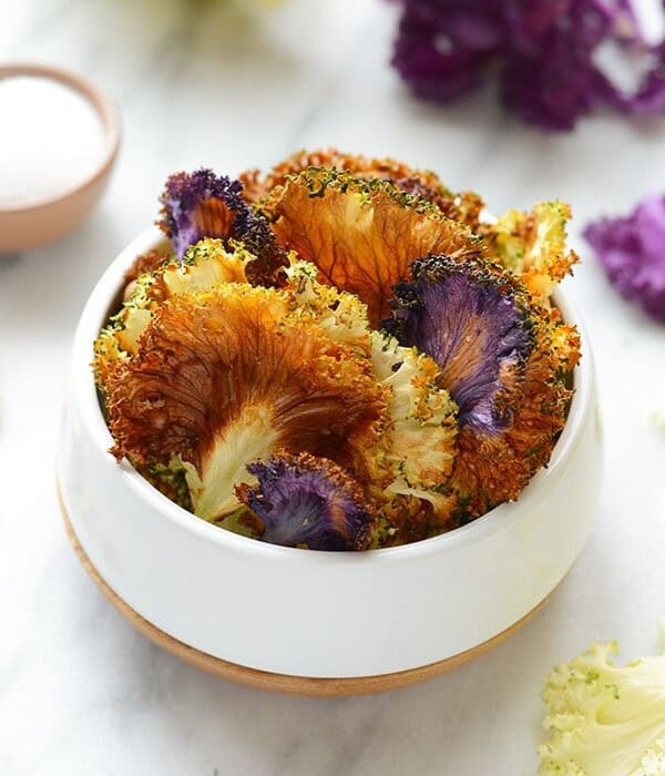 a white bowl with purple flowers and garlic roasted kale chips.