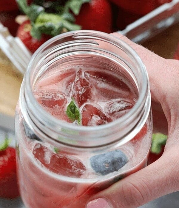 a hand holding a mason jar of strawberry lemonade Kombucha Mocktail.