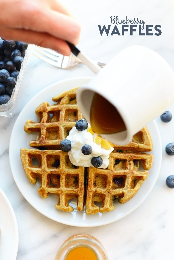 Syrup being poured on a blueberry waffle