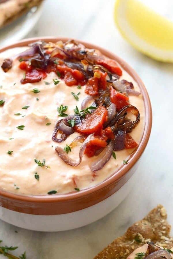 a bowl of skinny roasted red pepper and goat cheese dip with onions and tomatoes.