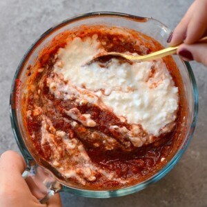 A person pouring sauce onto a Naked Spinach Quinoa Lasagna Casserole.