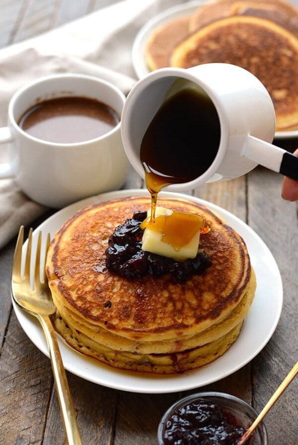 A person pouring syrup over whole wheat pancakes on a plate.