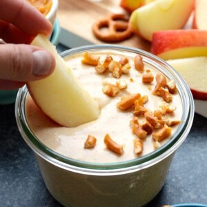 a person is dipping a pretzel into a bowl of pumpkin yogurt dip.