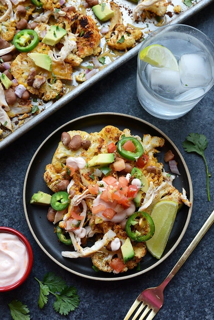 cauliflower nachos topped with pulses, rotisserie chicken, pico de gallo, and avocado on plate