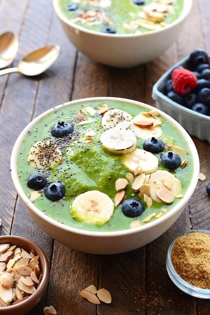 healthy green smoothie bowl topped with fruit and nuts and chia seeds