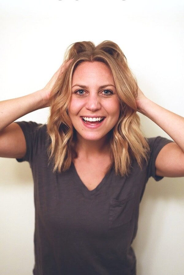 A woman demonstrating how to curl short hair using a flat iron, while striking a pose with her hands in her hair.