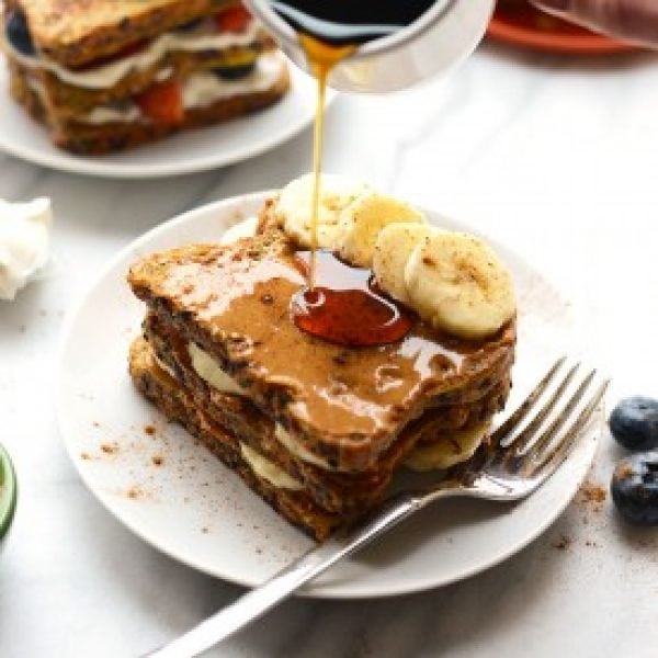 A stack of french toast with syrup being poured over it.