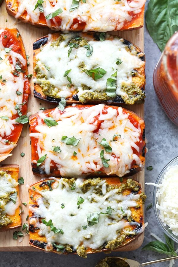 Roasted sweet potatoes topped with pesto and basil on a cutting board.