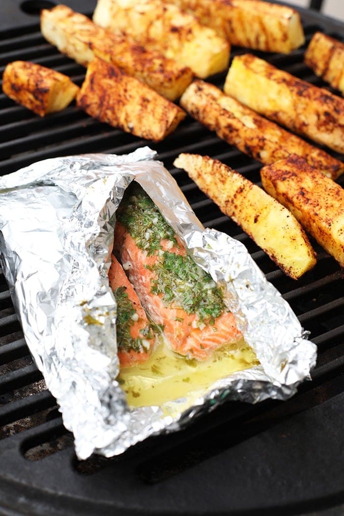 Salmon in a foil on the grill with pineapple next to it.