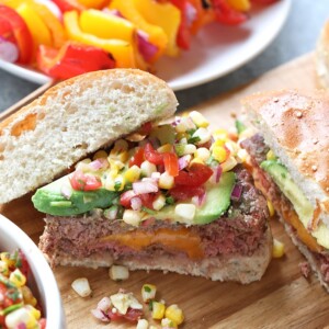 Mexican juicy lucys topped with avocado and corn on a cutting board.