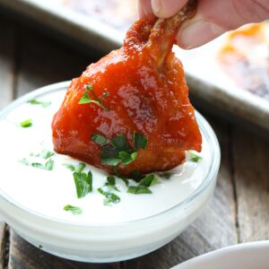 A person enjoying baked chicken wings by dipping them into a bowl of sauce.