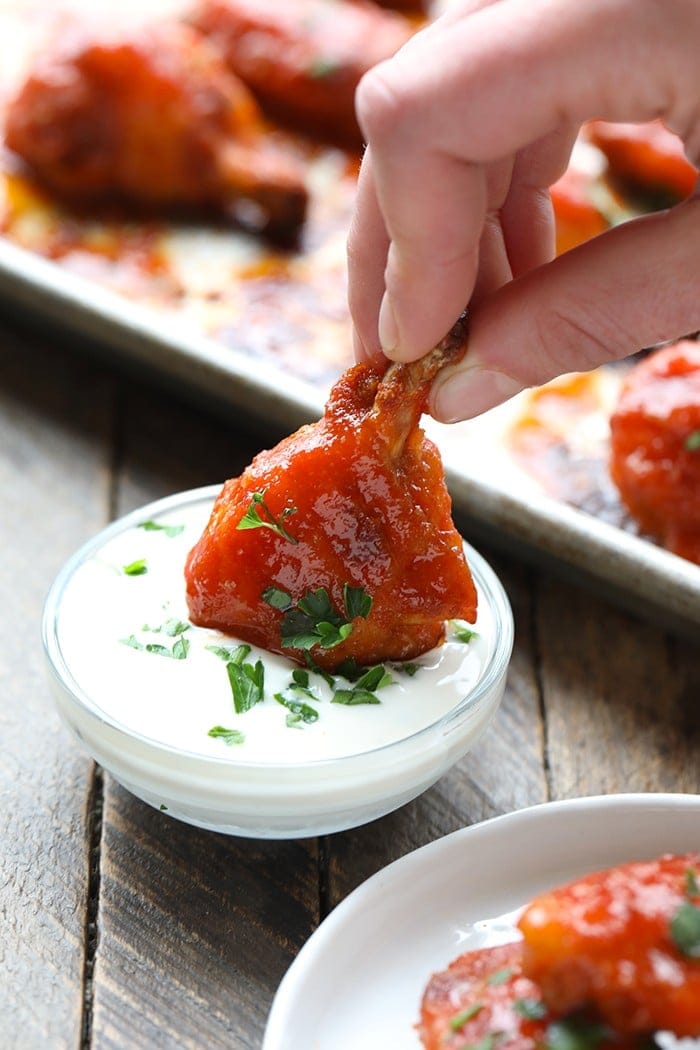 baked buffalo chicken wing being dipped in yogurt sauce