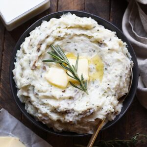 a bowl of healthy mashed potatoes with butter and a sprig of rosemary.