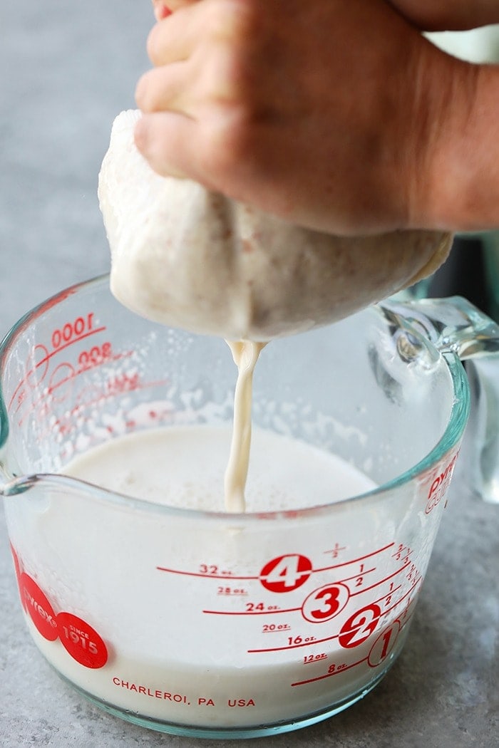 blended almond milk being strained through nut cloth to create smooth almond milk