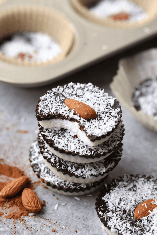 a stack of coconut butter cups with chocolate and almond filling in a muffin tin.