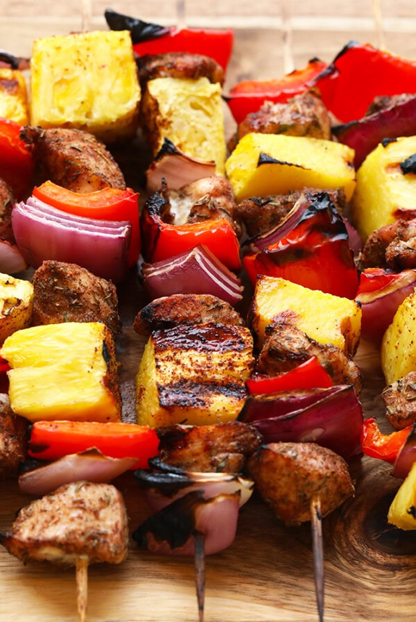 jerk chicken skewers with grilled pineapple on a wooden cutting board.