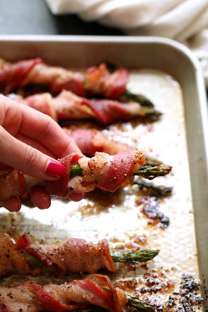 a hand holding bacon wrapped asparagus