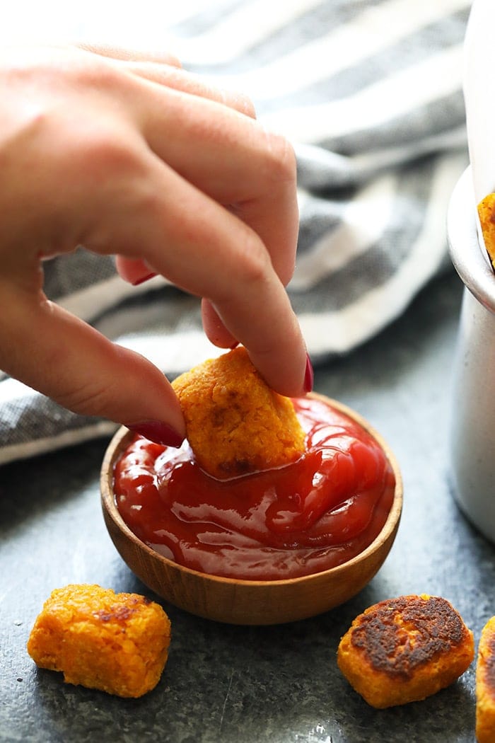 A hand dipping a tater tot into ketchup.