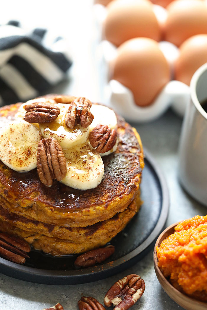 Paleo pumpkin pancakes on a plate topped with bananas and pecans.