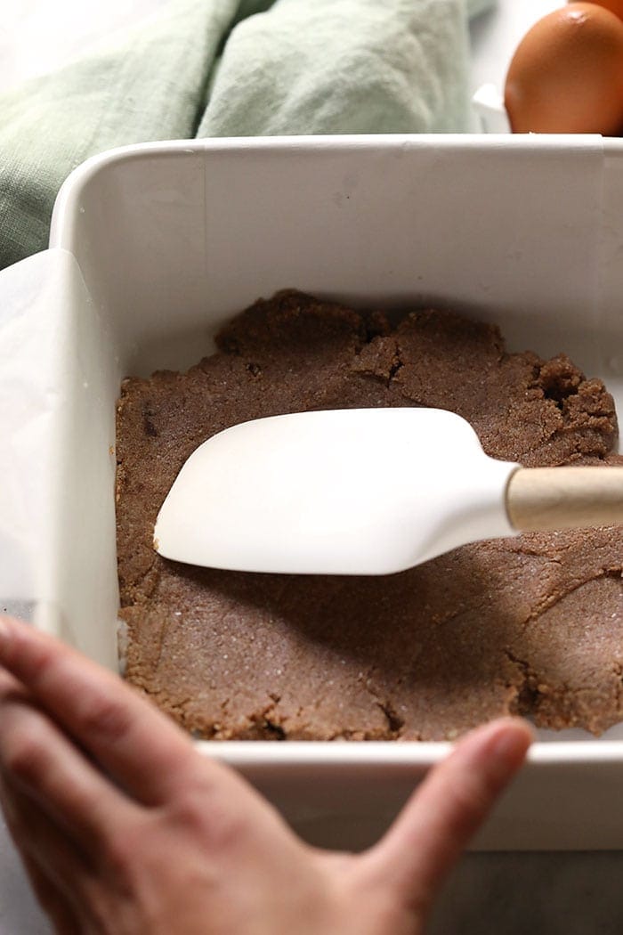 A pair of hands using a spatula to spread pumpkin pie crust to the bottom of a pan