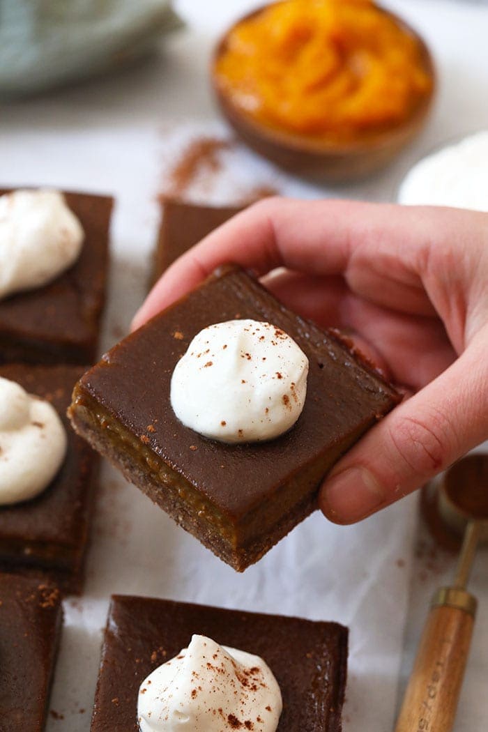 A hand holding a pumpkin pie bar with whipped cream topping