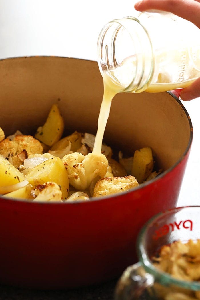 roasted potatoes and cauliflower with chicken broth being poured on it