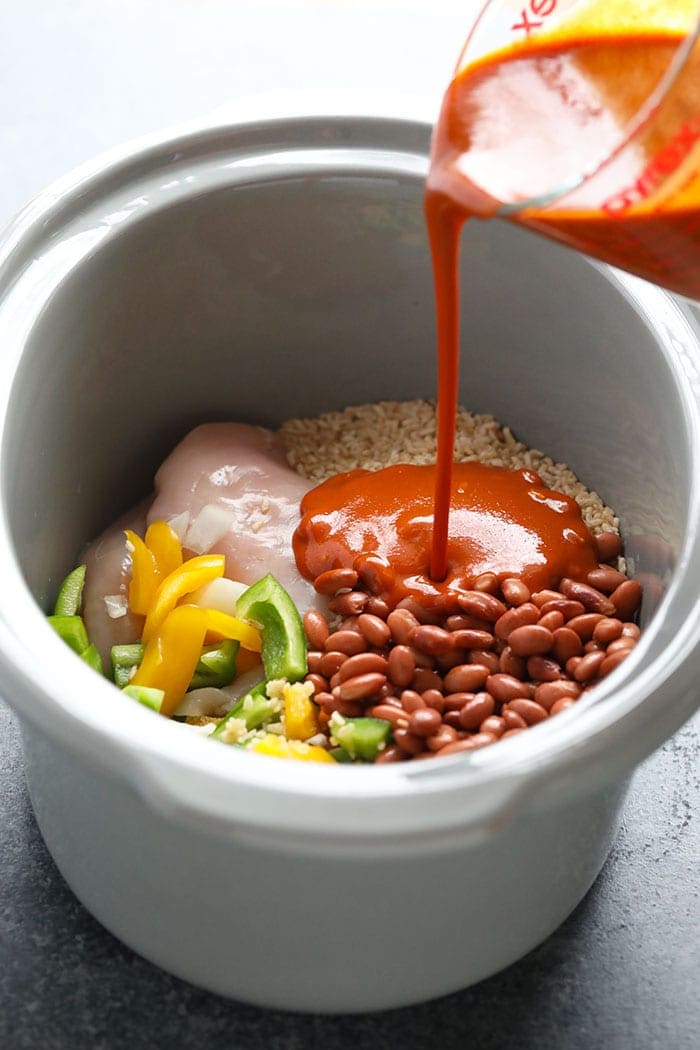 Pouring enchilada sauce into a slow cooker.