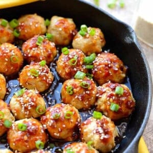 A skillet filled with cooked Kung Pao Chicken Meatballs garnished with sesame seeds and chopped green onions.