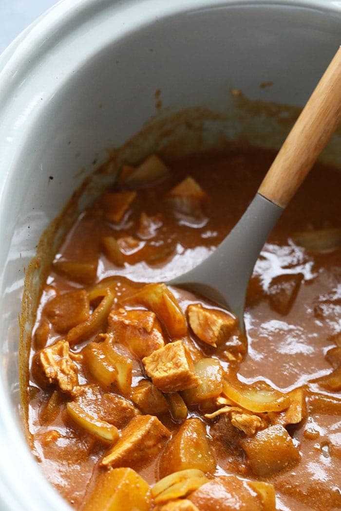 slow cooker chicken tikka masala in a crock pot being stirred with a spoon