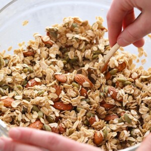 A person preparing a healthy granola recipe in a glass bowl.