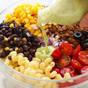 pouring dressing on top of pasta salad.