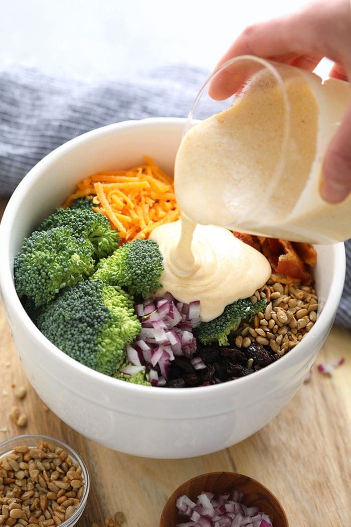 Pouring sauce for healthy broccoli salad onto ingredients.