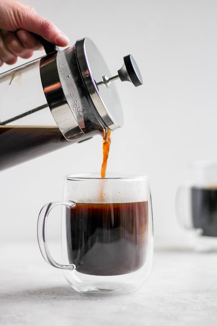 Pouring coffee from a french press into a mug.