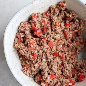 a white bowl with a black bean burger and peppers.