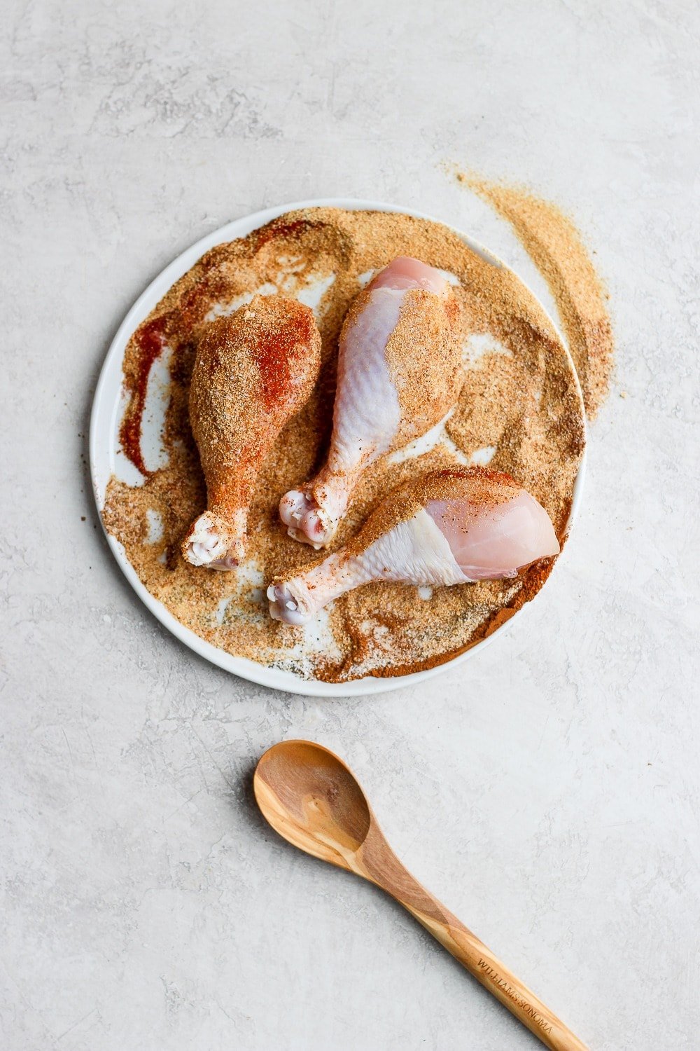 chicken legs rolled in dry rub on a plate ready to be grilled