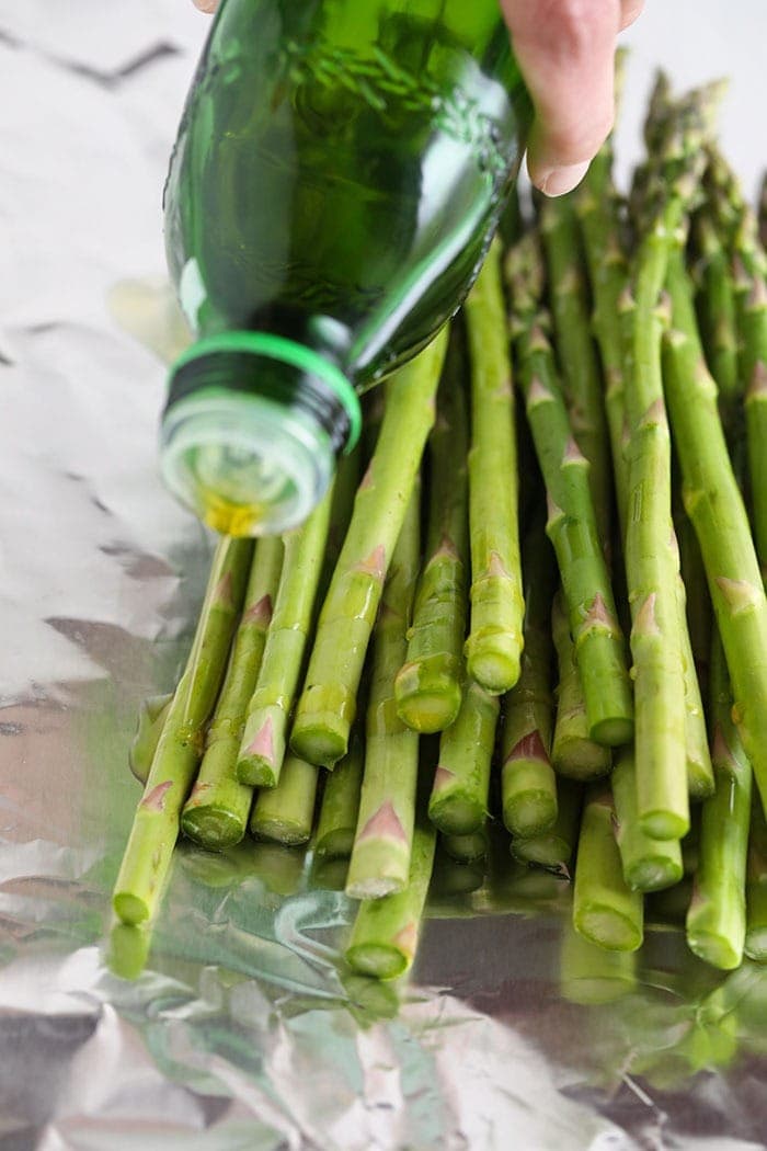 drizzling olive oil on asparagus .