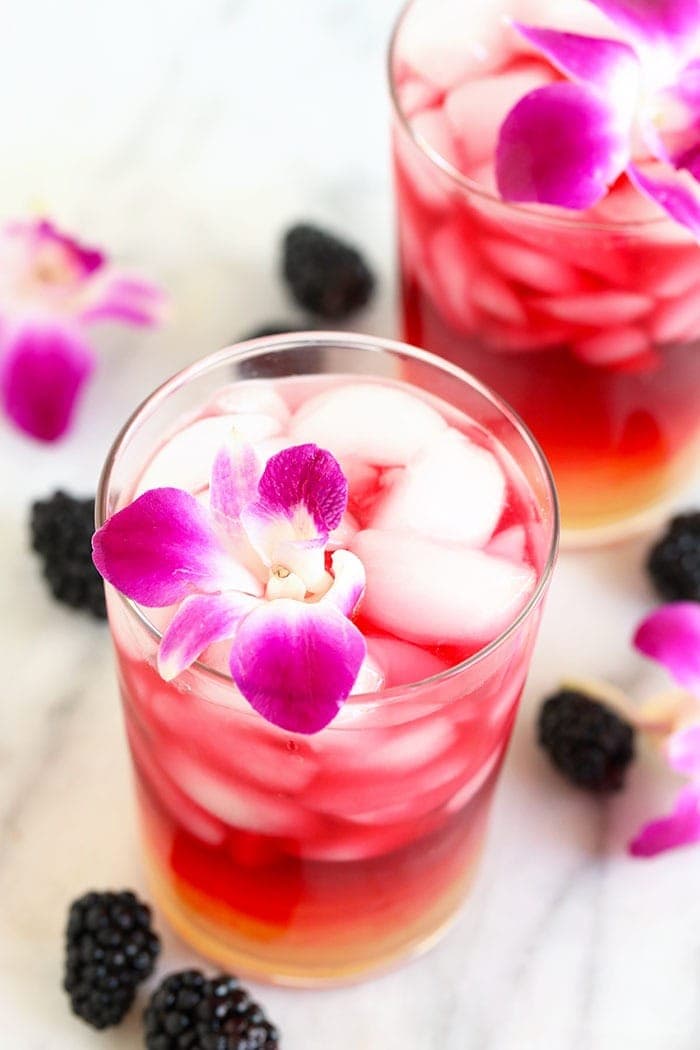 arnold palmer drink in a glass with an edible flower surrounded by blackberries