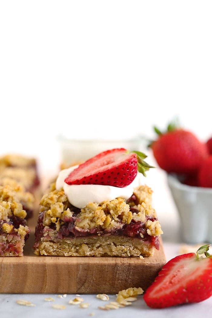 strawberry oatmeal bar sliced and topped with whipped cream and a sliced fresh strawberry