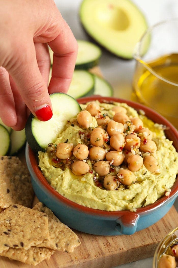 Dipping cucumber into avocado hummus